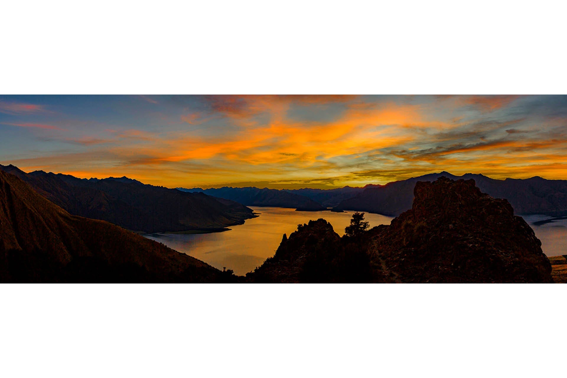 Tranquil sunrise over Lake Hawea in New Zealand's South Island, with soft golden light reflecting on pristine waters and surrounding Otago peaks
